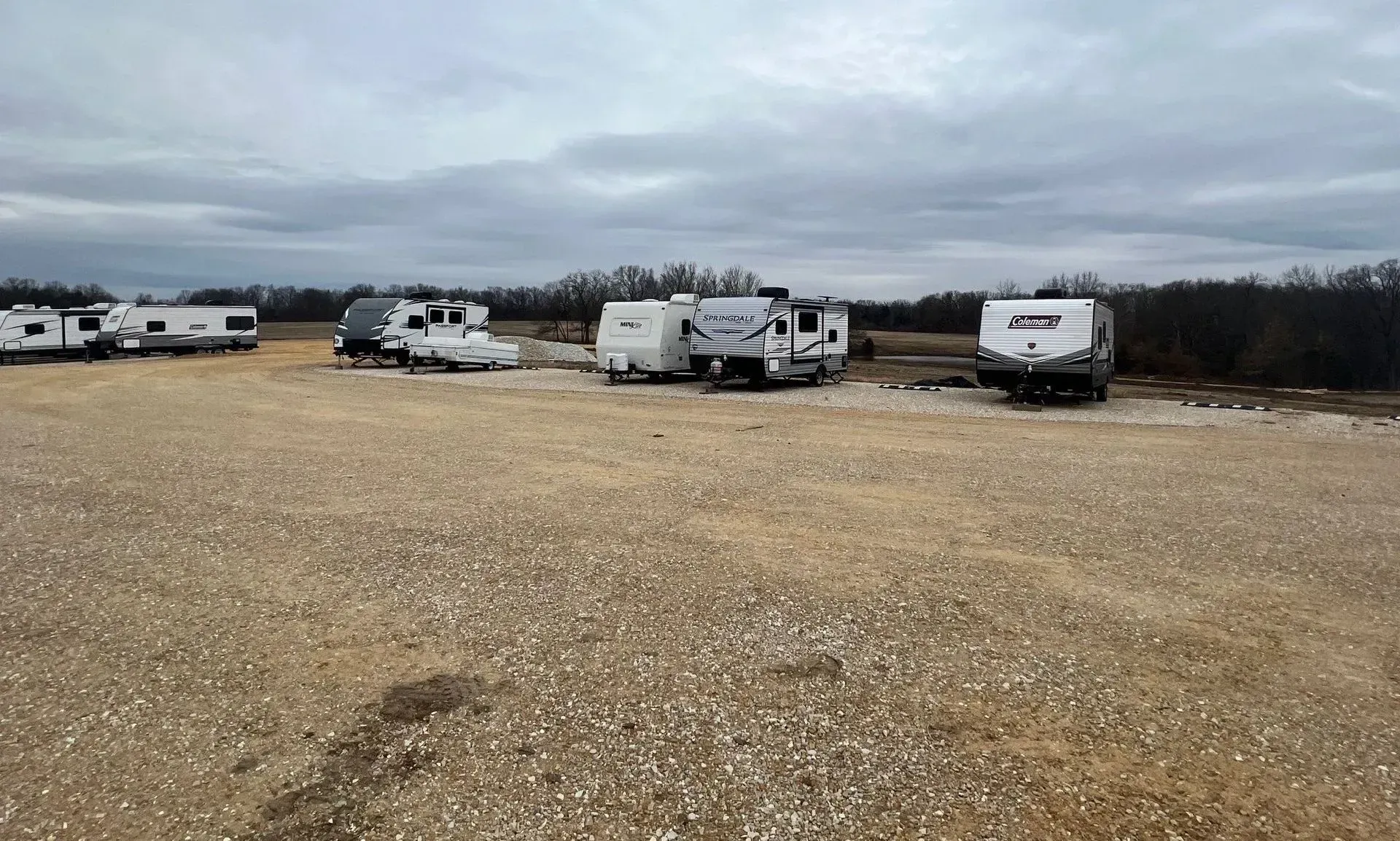 A row of rvs are parked in a gravel lot.