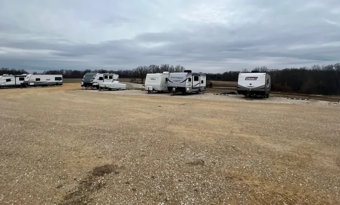 A row of rvs are parked in a gravel lot.