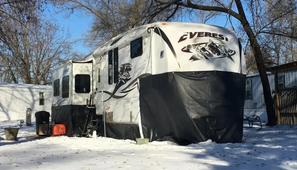 A white and black rv is parked in the snow.