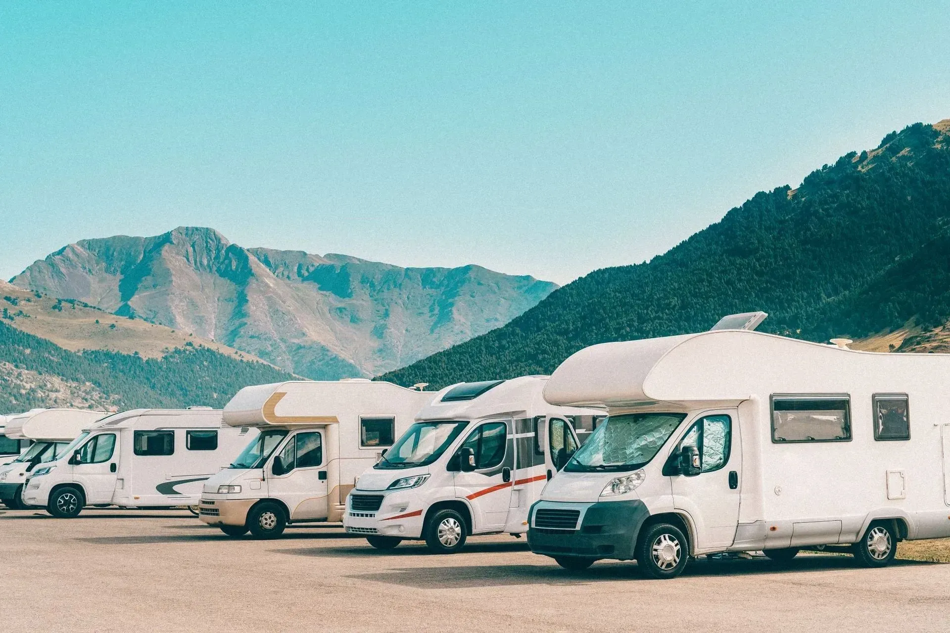 A row of rvs are parked in a parking lot with mountains in the background.