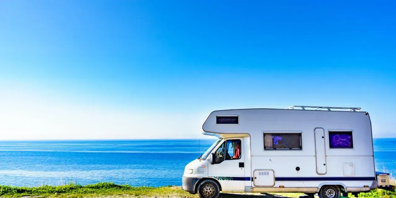 A white rv is parked on a hill near the ocean.