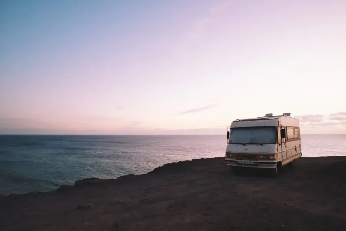 A camper van is parked on the shore of the ocean at sunset.