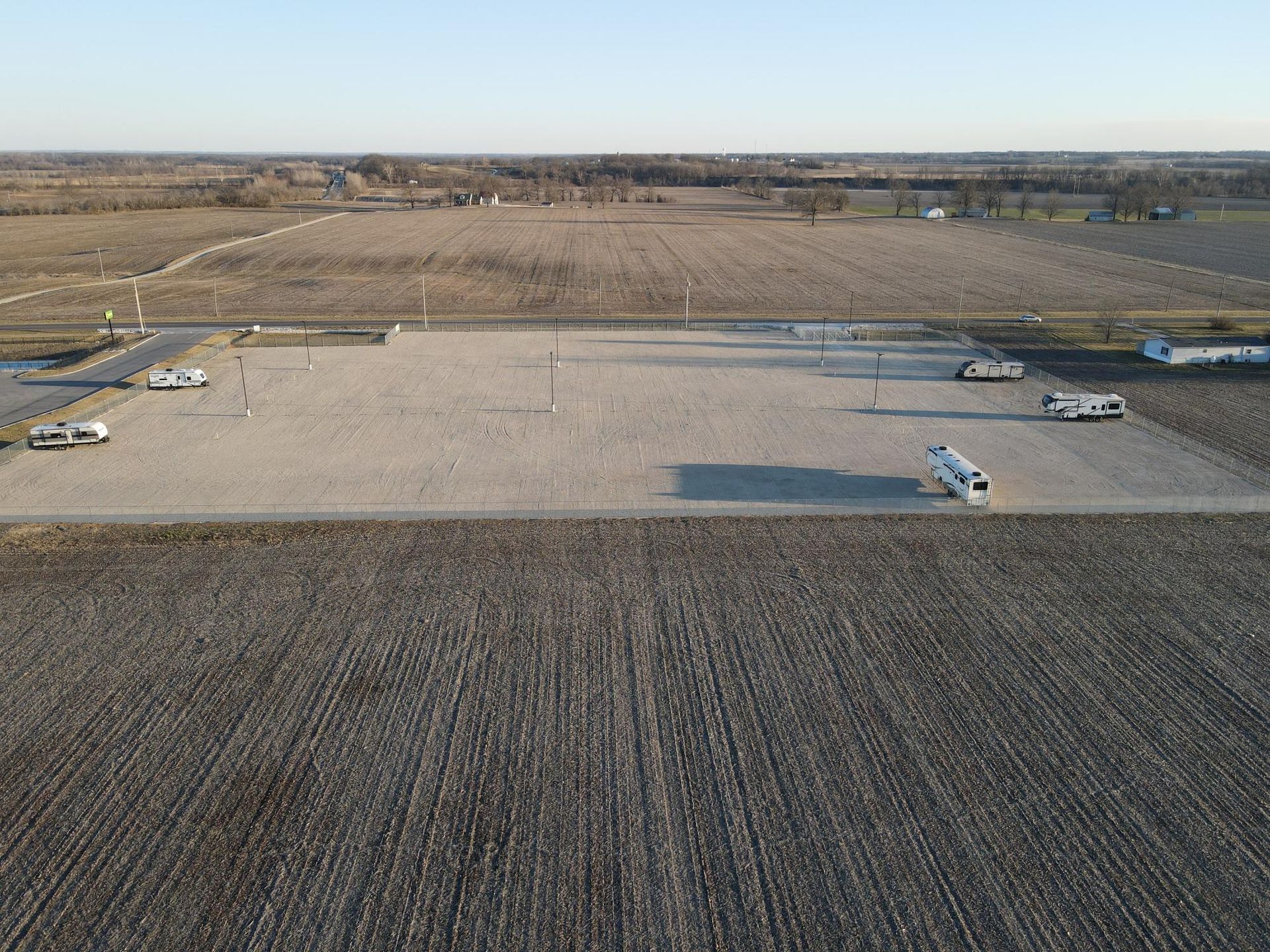 Overview of a gravel lot with parked vehicles in a harvested field, under a clear sky.
