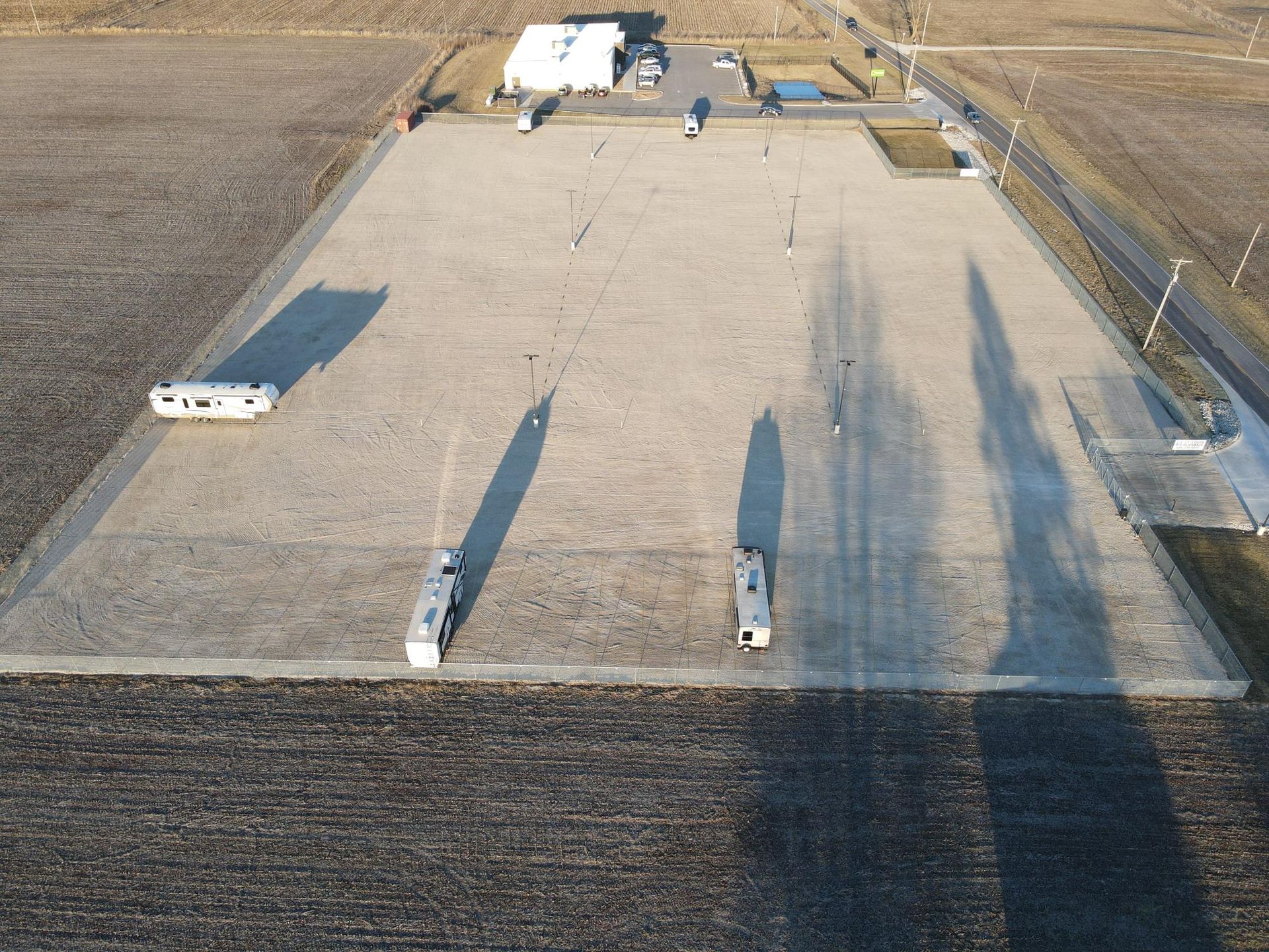 Aerial view of a gravel lot with RVs parked on it, surrounded by farm fields and buildings.
