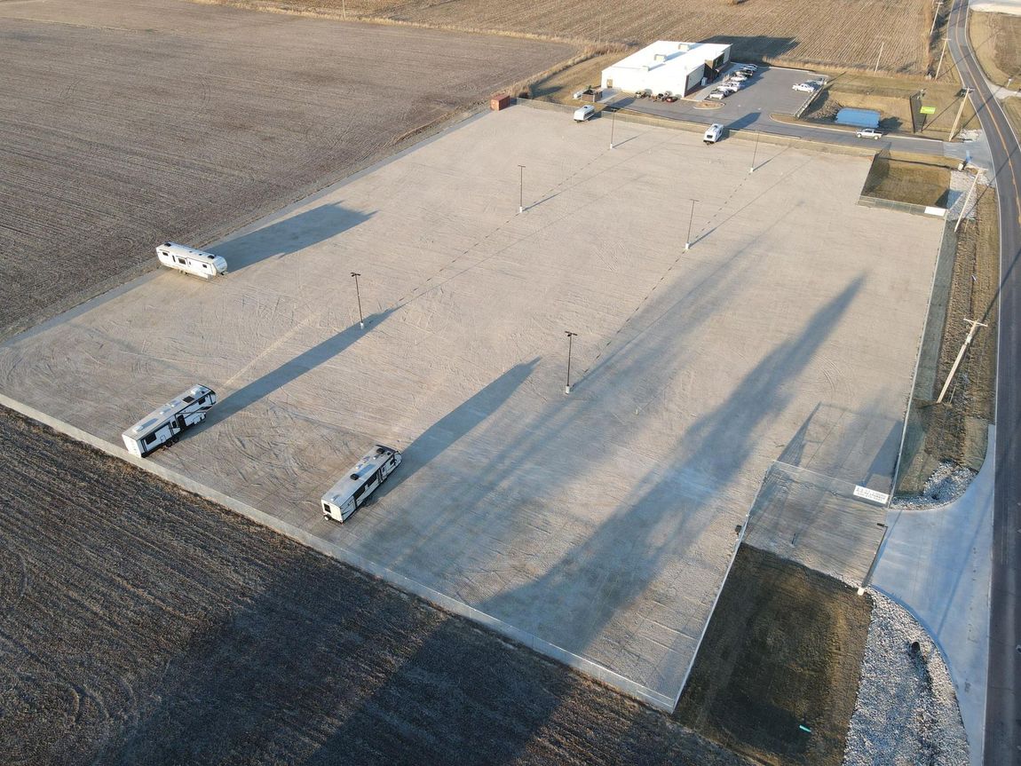 Aerial view of a gravel parking lot with three RVs, a building, and a road.