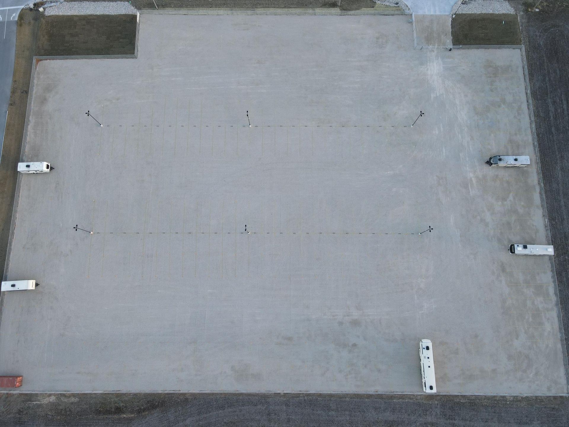 An aerial view of a rectangular, light-colored gravel lot with a few scattered parked RVs and utility hookups.