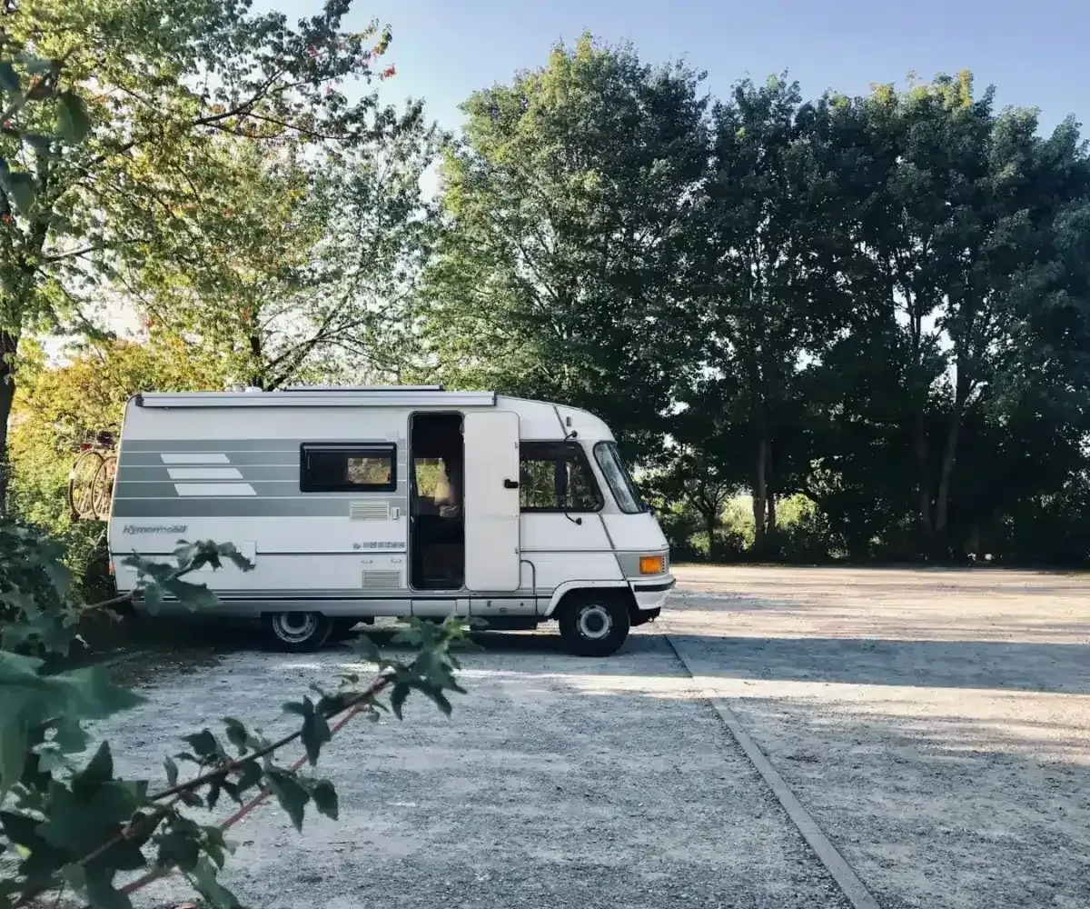 A white rv is parked in a parking lot surrounded by trees.
