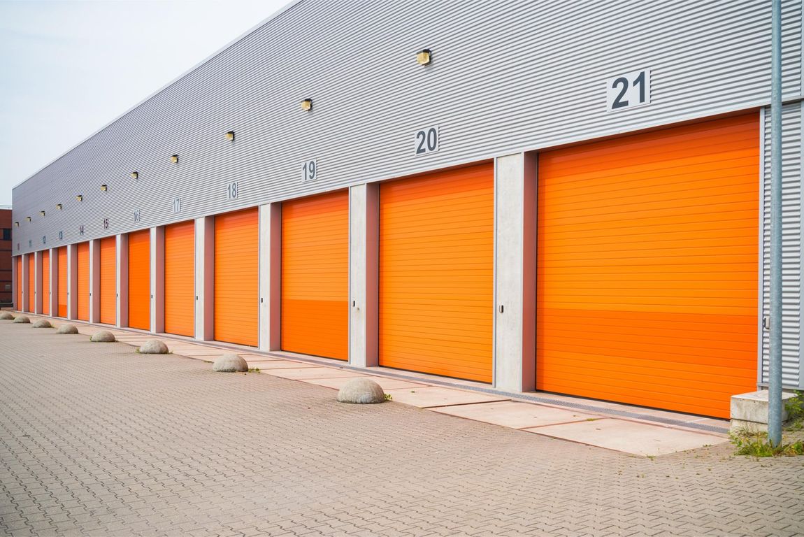 Row of orange storage unit doors along a brick paved building exterior; numbers 13-21 visible.