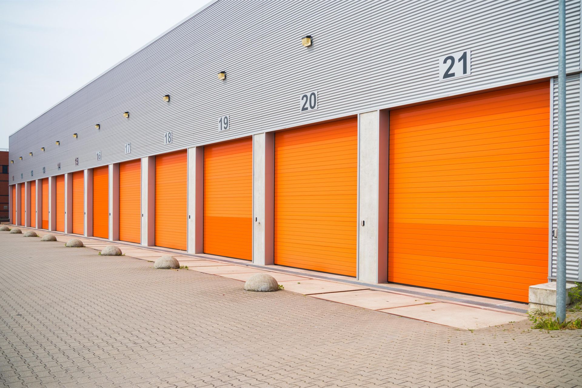 Row of orange storage unit doors along a gray building with numbered units.