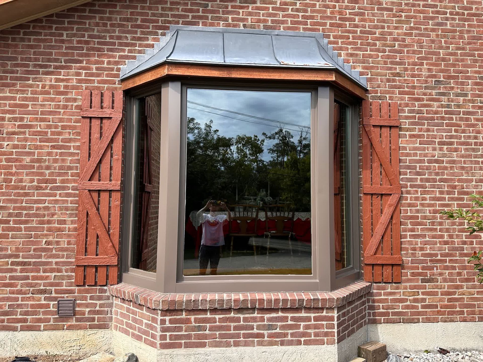 Bay window with red brick exterior, brown trim, shutters, and a reflective glass.