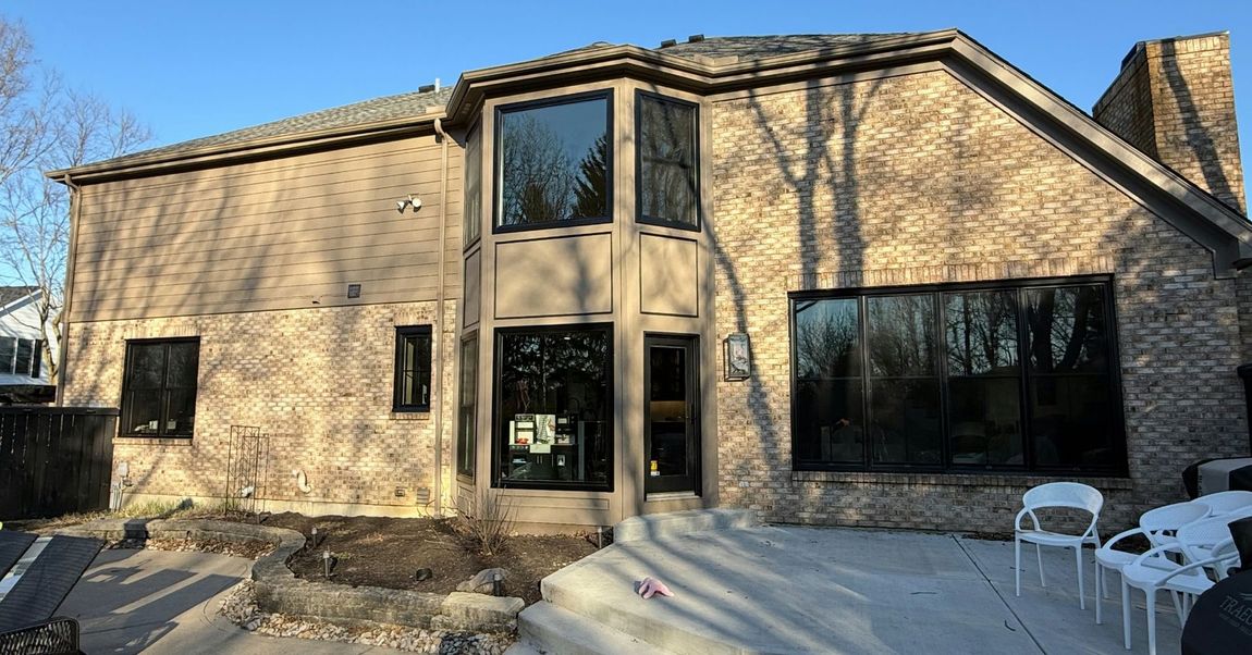 Brick house with large dark windows, a concrete patio, and a clear blue sky.