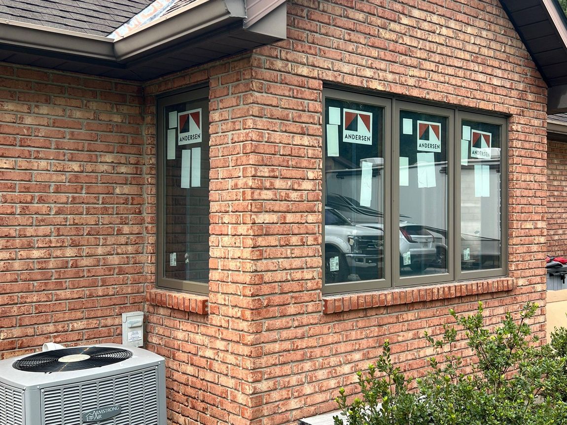 Brick house exterior with new brown framed windows, showing reflections of vehicles.