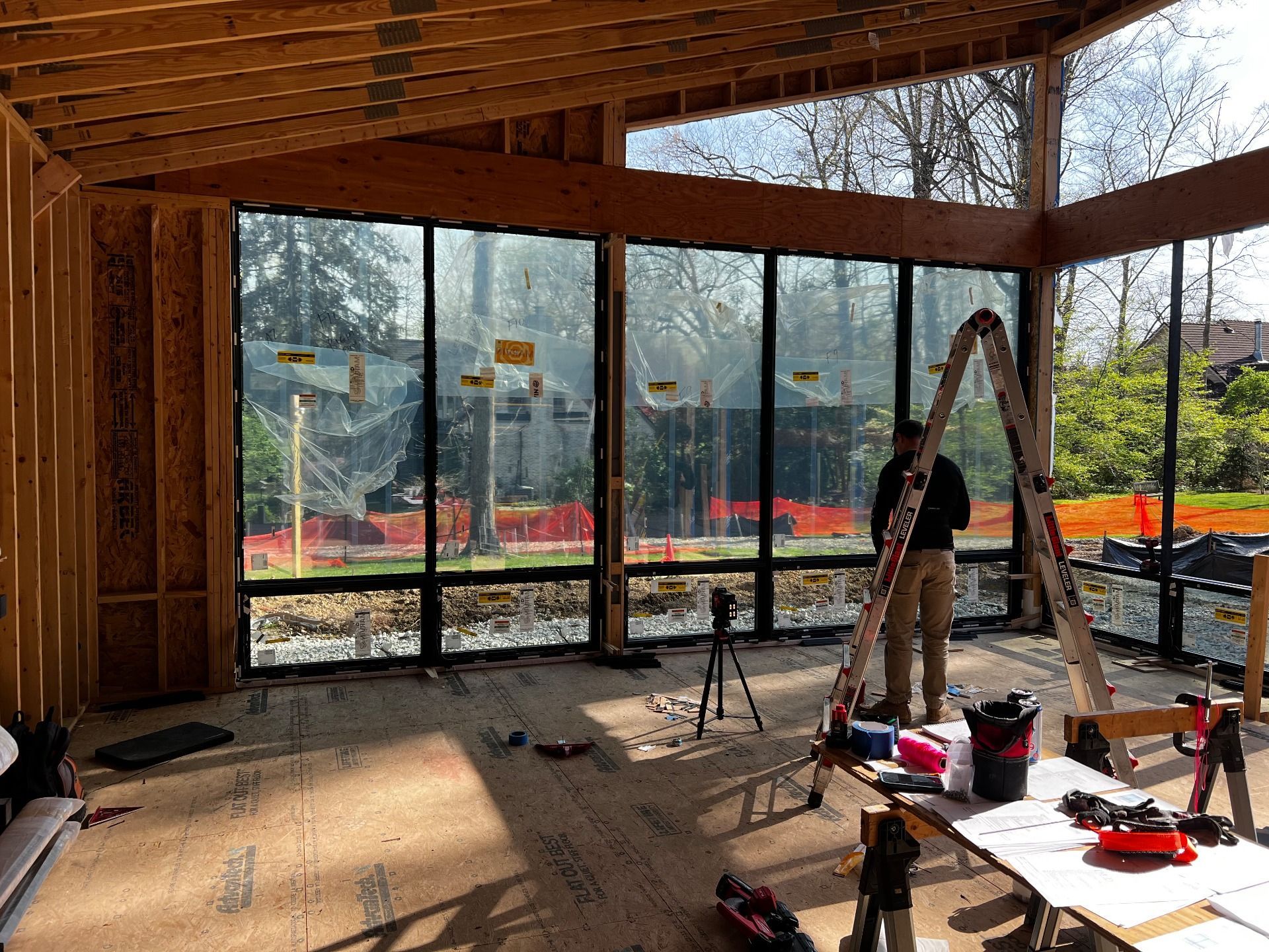 Construction worker inside a wood-framed building with large windows; outdoors visible.