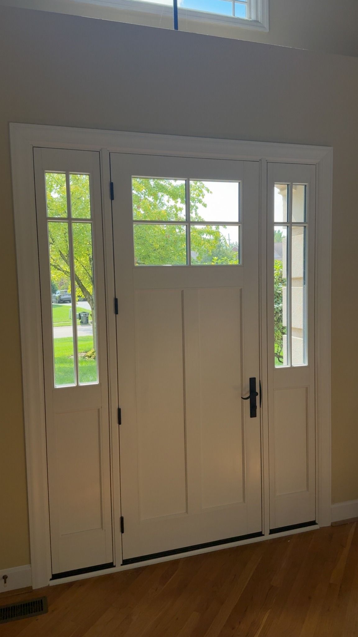 White front door with sidelights and transom window, framing the outside view.