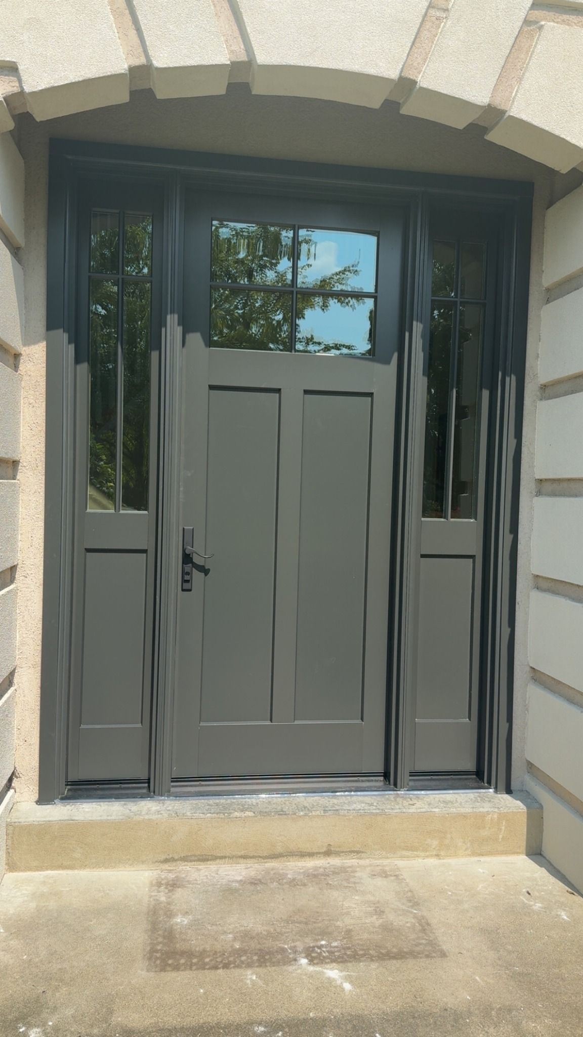 Gray door with glass panel above, sidelights, and decorative bars, set in stone archway.