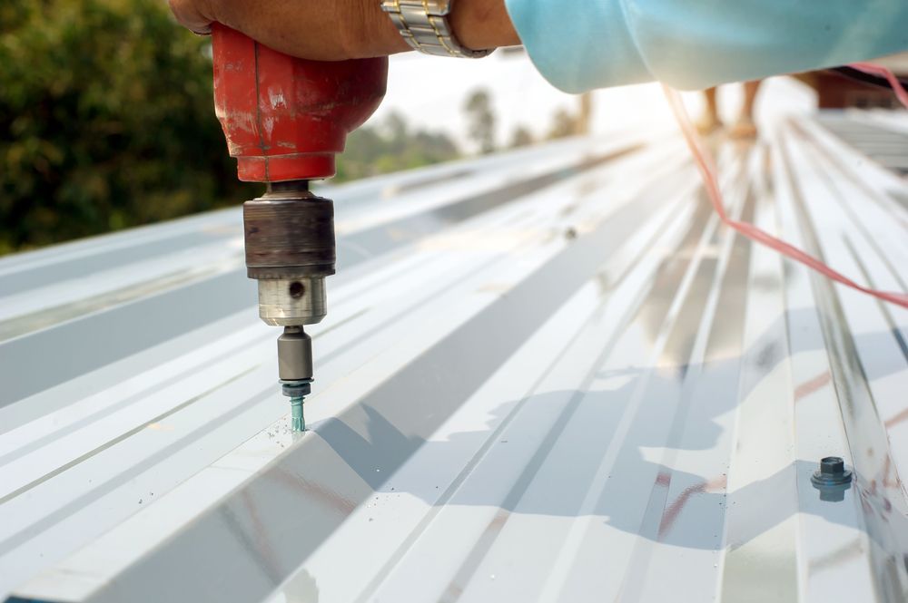Person Using a Red Drill to Secure a Sheet of Corrugated Metal Roofing — MJD Roofing Sunshine Coast in Cooroy, QLD