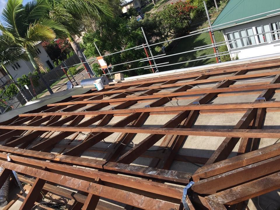 Wooden Roof Frame Under Construction With a Green-roofed Building — MJD Roofing Sunshine Coast in Cooroy, QLD