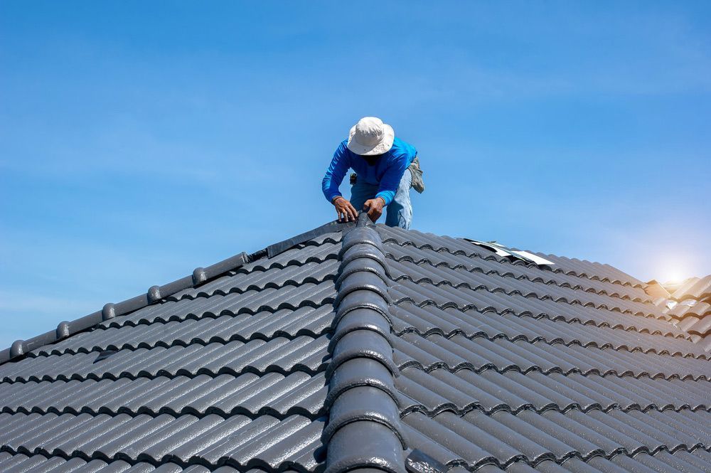 Roofer in Blue Shirt and White Hat Working on a Gray Tiled Roof — MJD Roofing Sunshine Coast in Cooroy, QLD