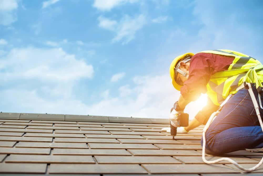 Roofer on a Roof, Wearing a Safety Vest and Hardhat, Using a Drill — MJD Roofing Sunshine Coast in Cooroy, QLD