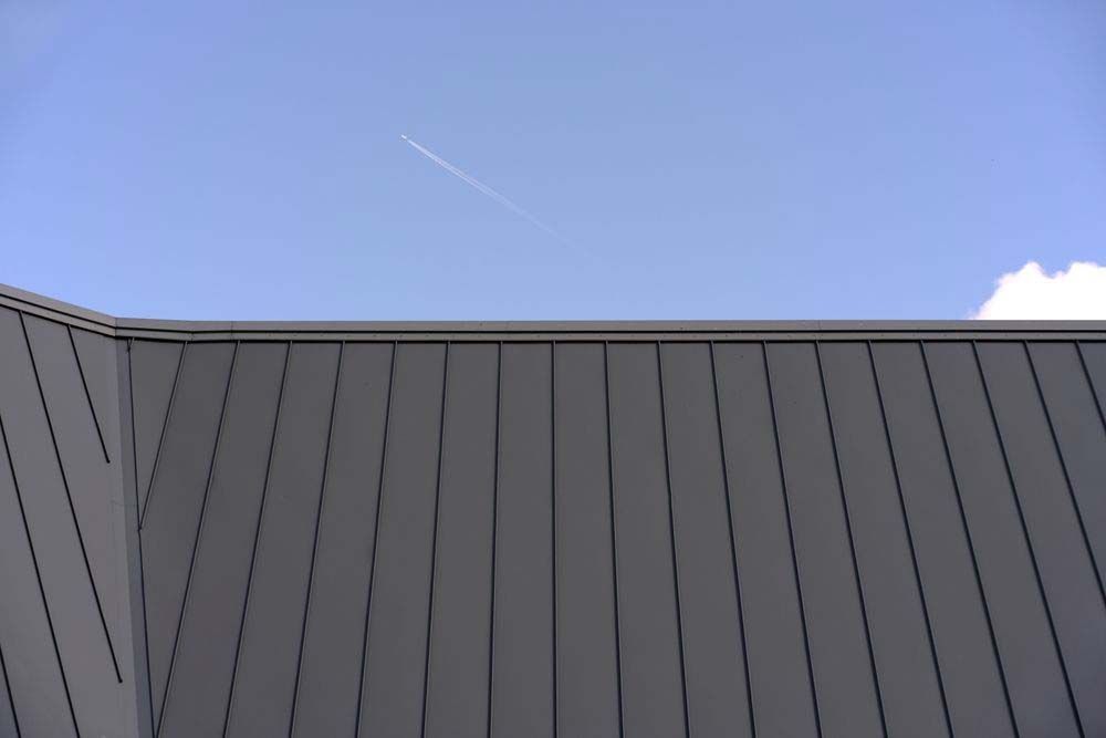 Dark Gray Metal Roof Against a Light Blue Sky With a Contrail — MJD Roofing Sunshine Coast in Cooroy, QLD