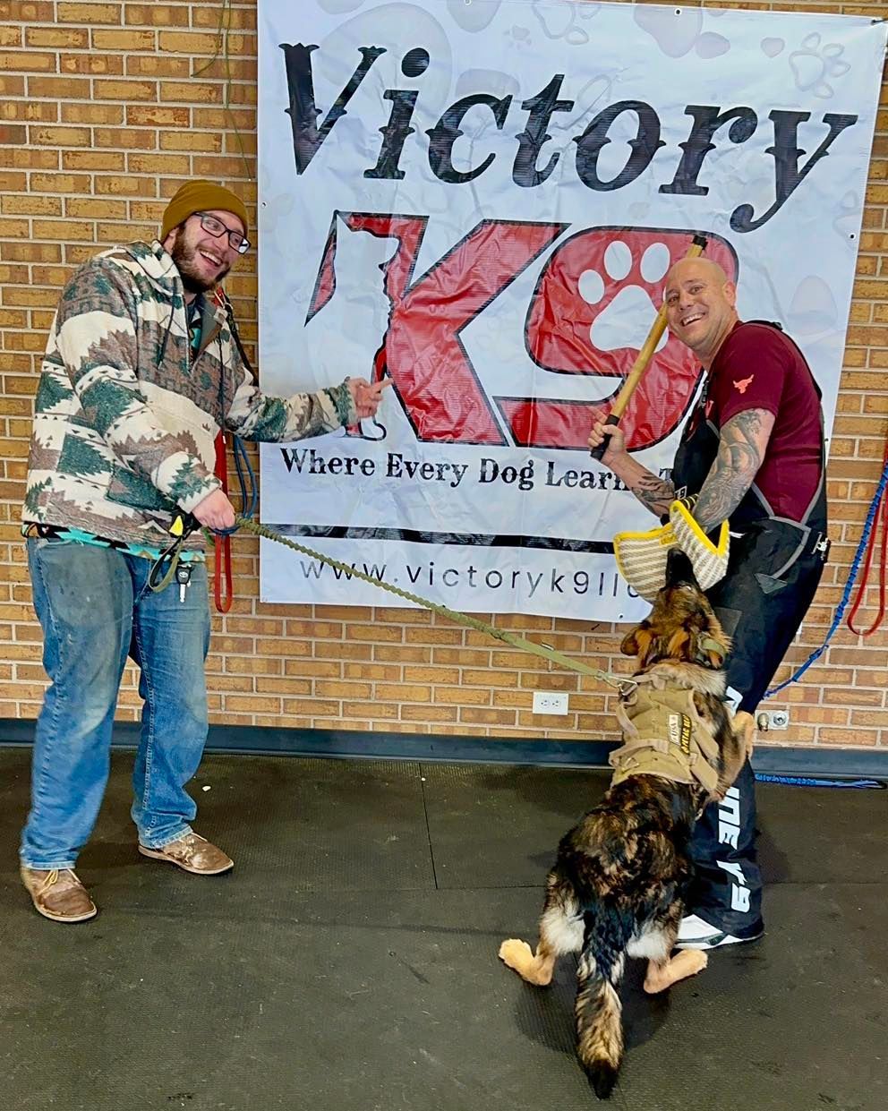 Two men are standing next to a dog in front of a sign that says victory k9