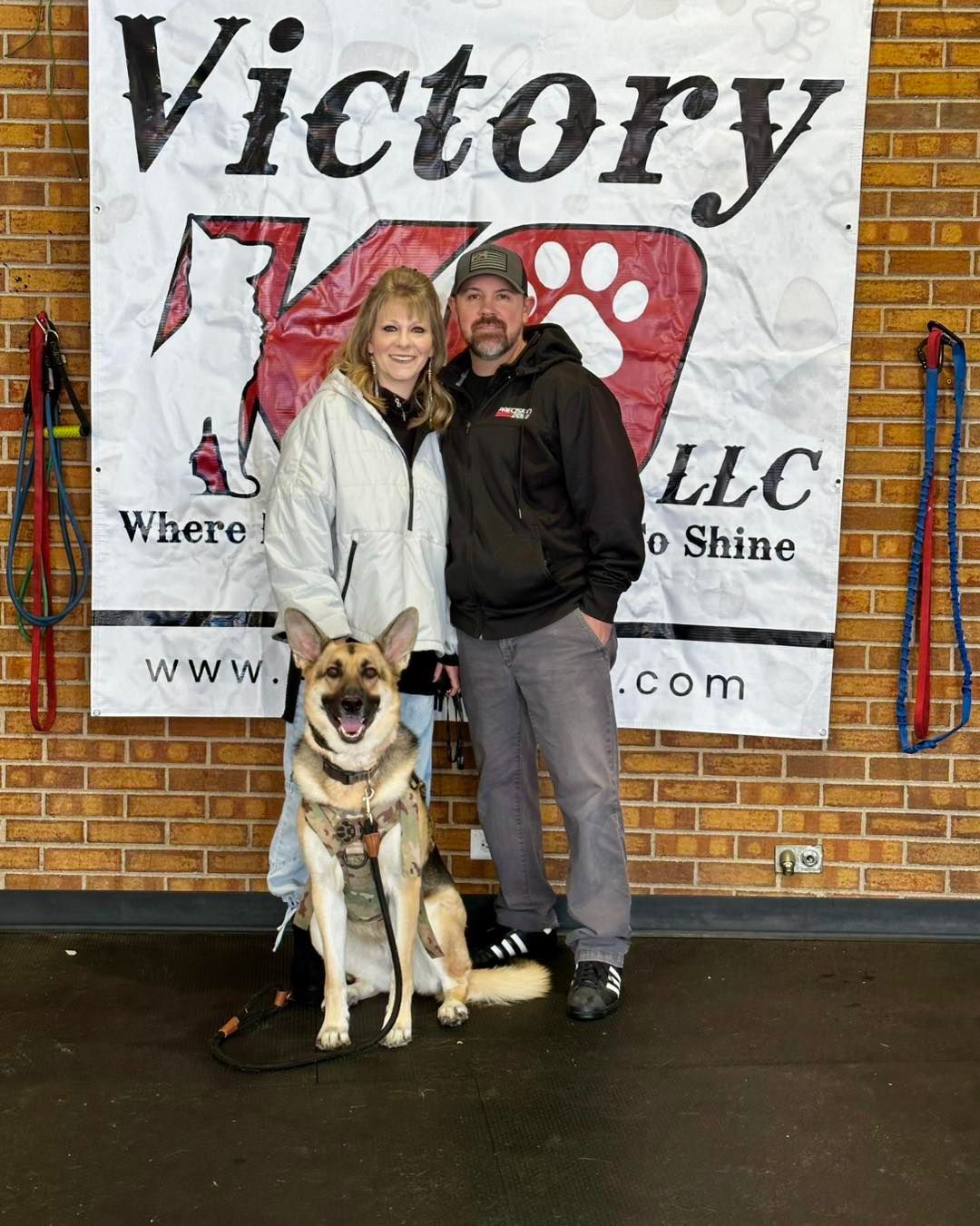 A man and woman standing next to a dog in front of a sign that says victory k9
