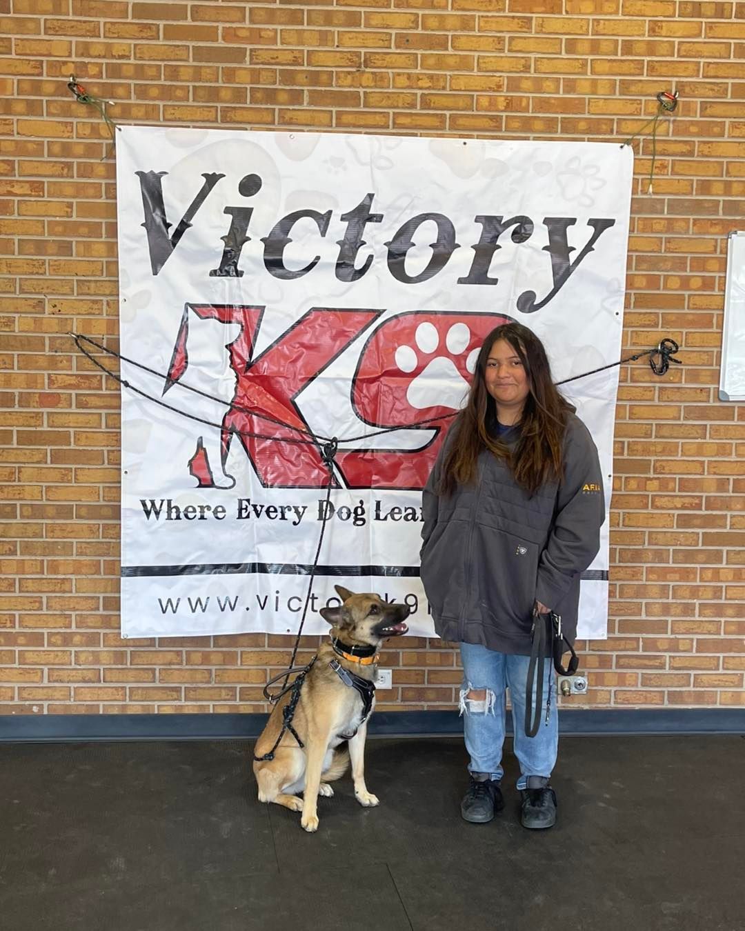 A woman is standing next to a dog in front of a victory k9 sign.