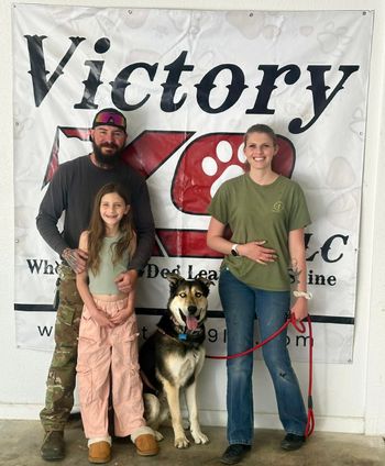 A family poses with their dog in front of a victory k9 sign
