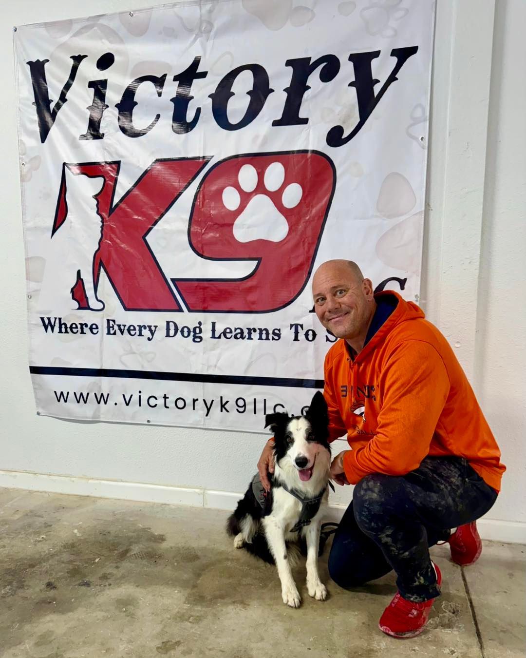 A man kneeling down with a dog in front of a victory k9 sign