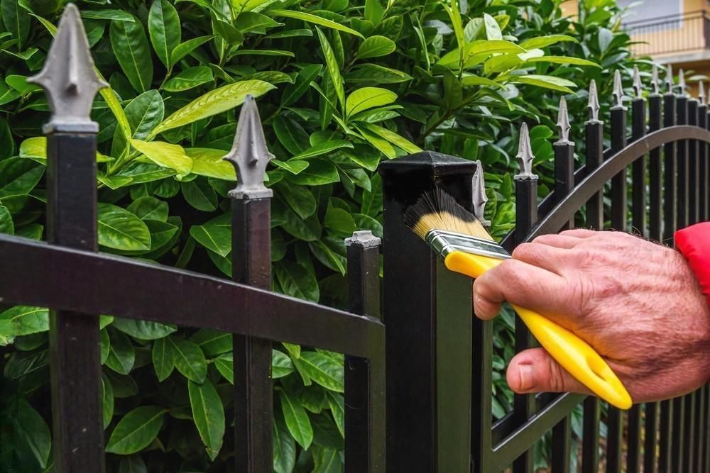 A person is painting a metal fence with a brush.