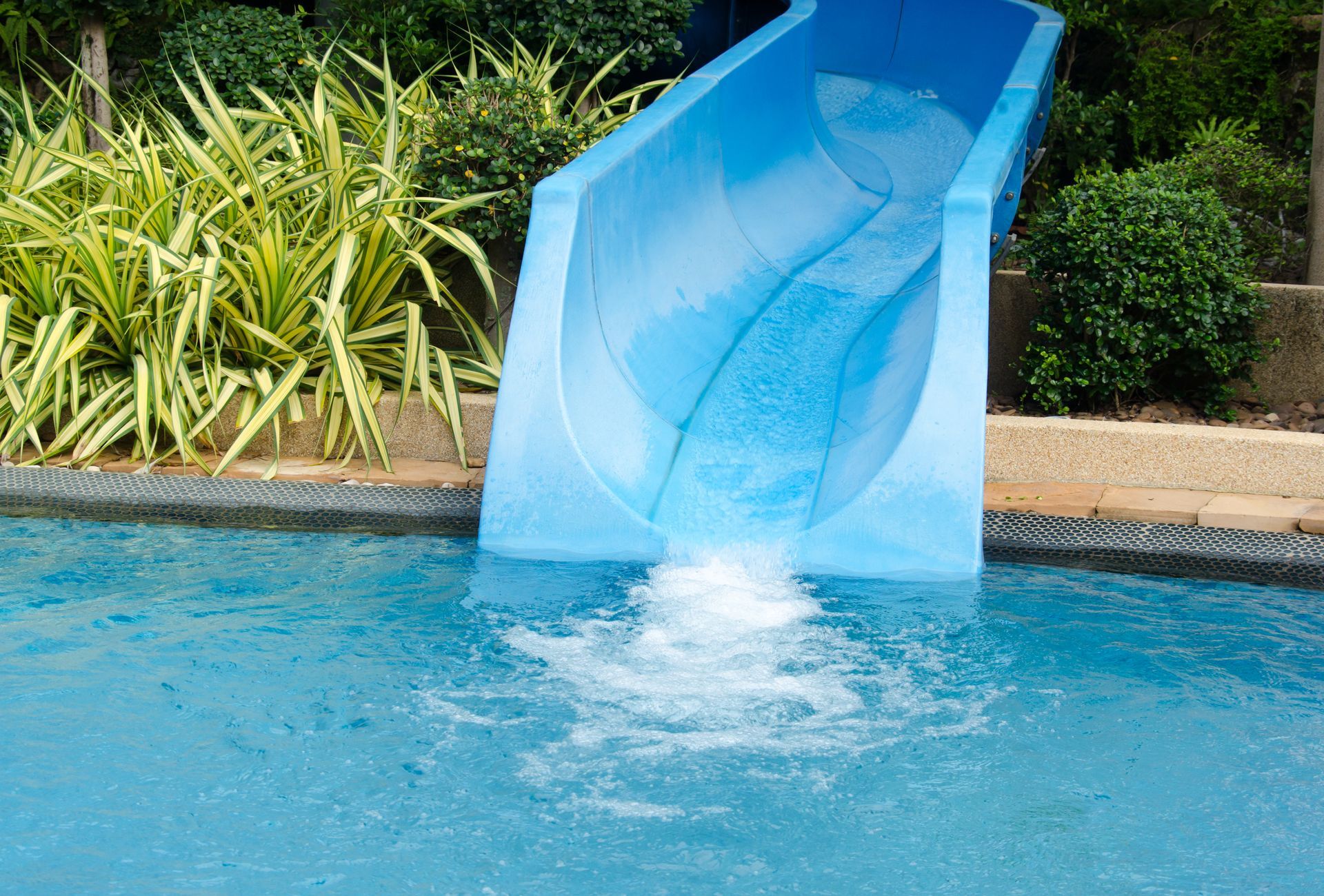 A blue water slide is going down a swimming pool.