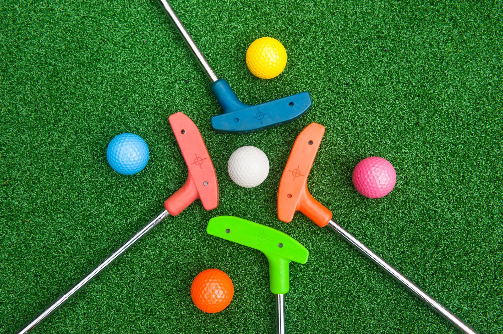A group of mini golf balls and putters on a green field.