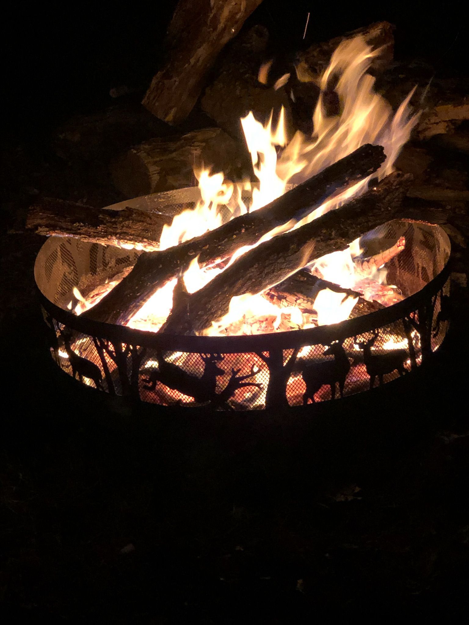 A fire pit filled with logs is lit up at night.