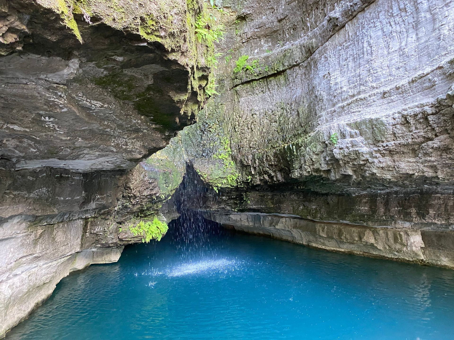 A waterfall is coming out of a cave into a pool of blue water.