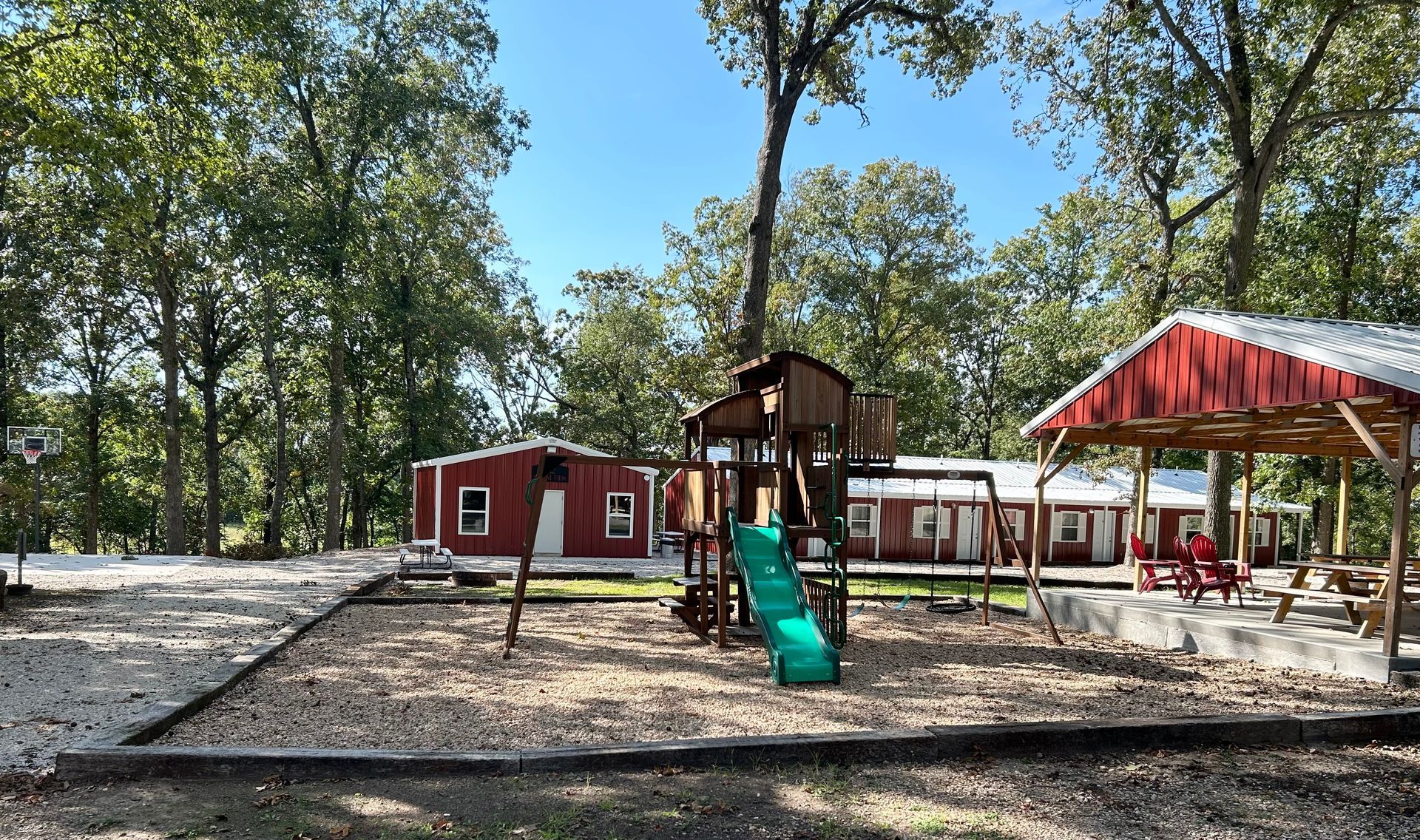 A playground with a slide and swings in front of a red barn.