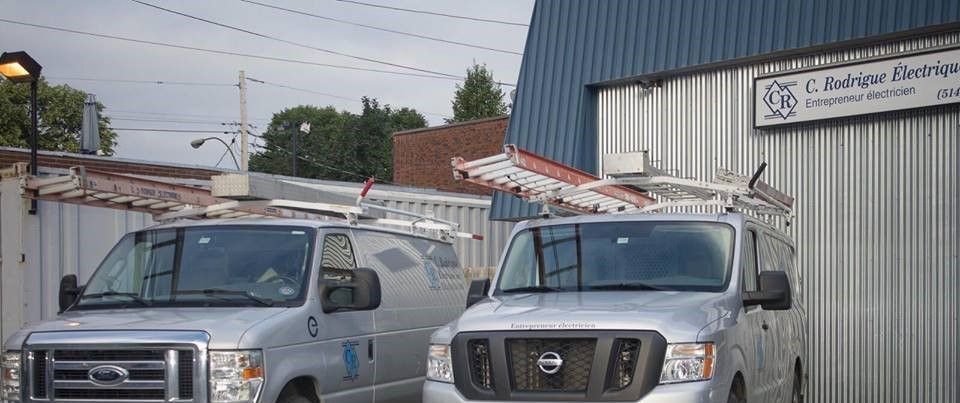 Deux camionnettes de travail argentées garées devant un bâtiment avec une pancarte d'entreprise.