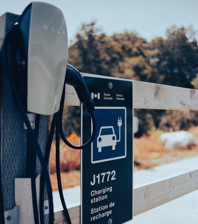 Borne de recharge pour véhicule électrique avec panneau J1772; extérieur, panneau bleu et blanc, câble de recharge et drapeau canadien.