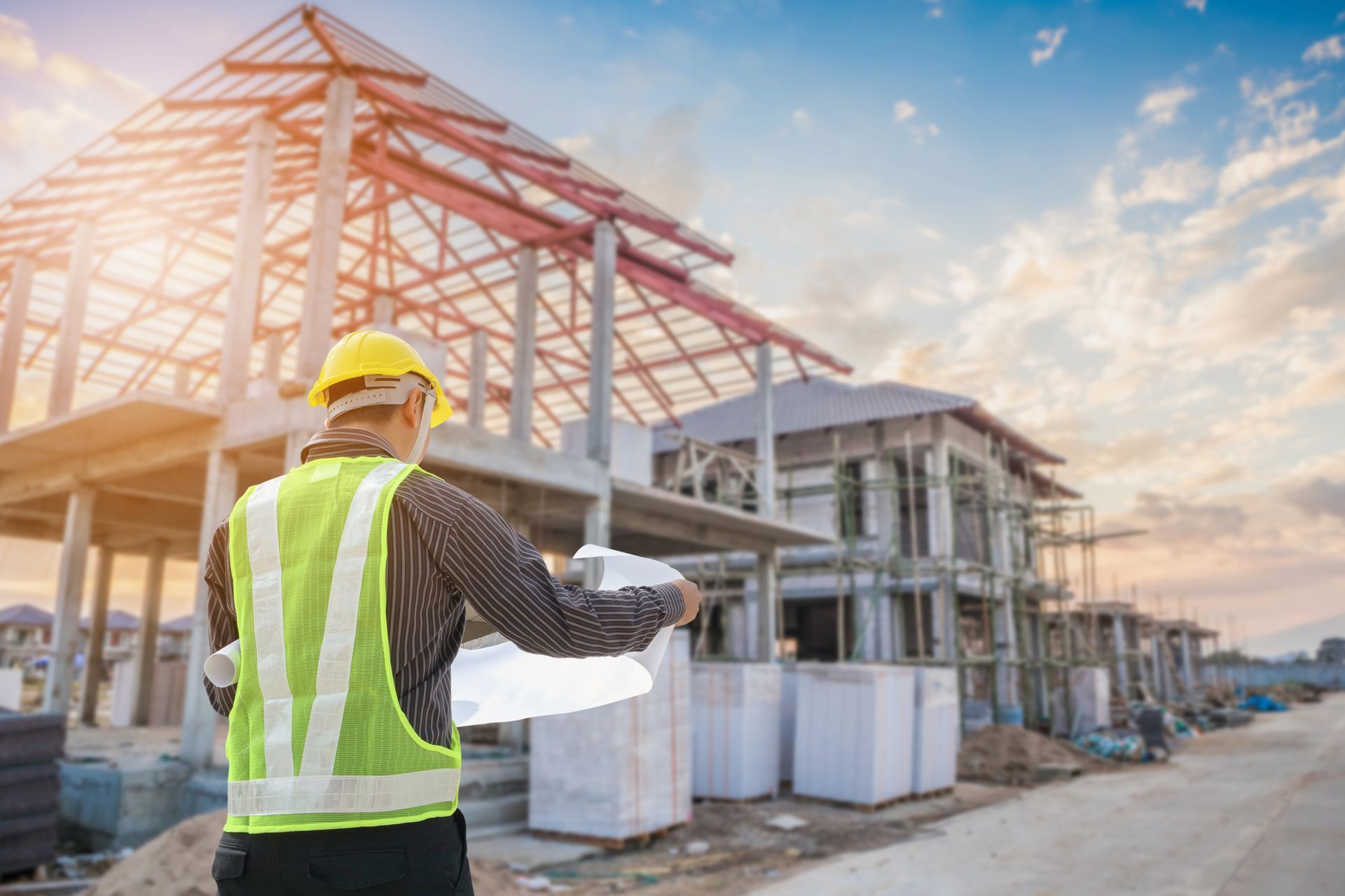 Construction worker in yellow helmet and vest reviewing blueprints on a building site.