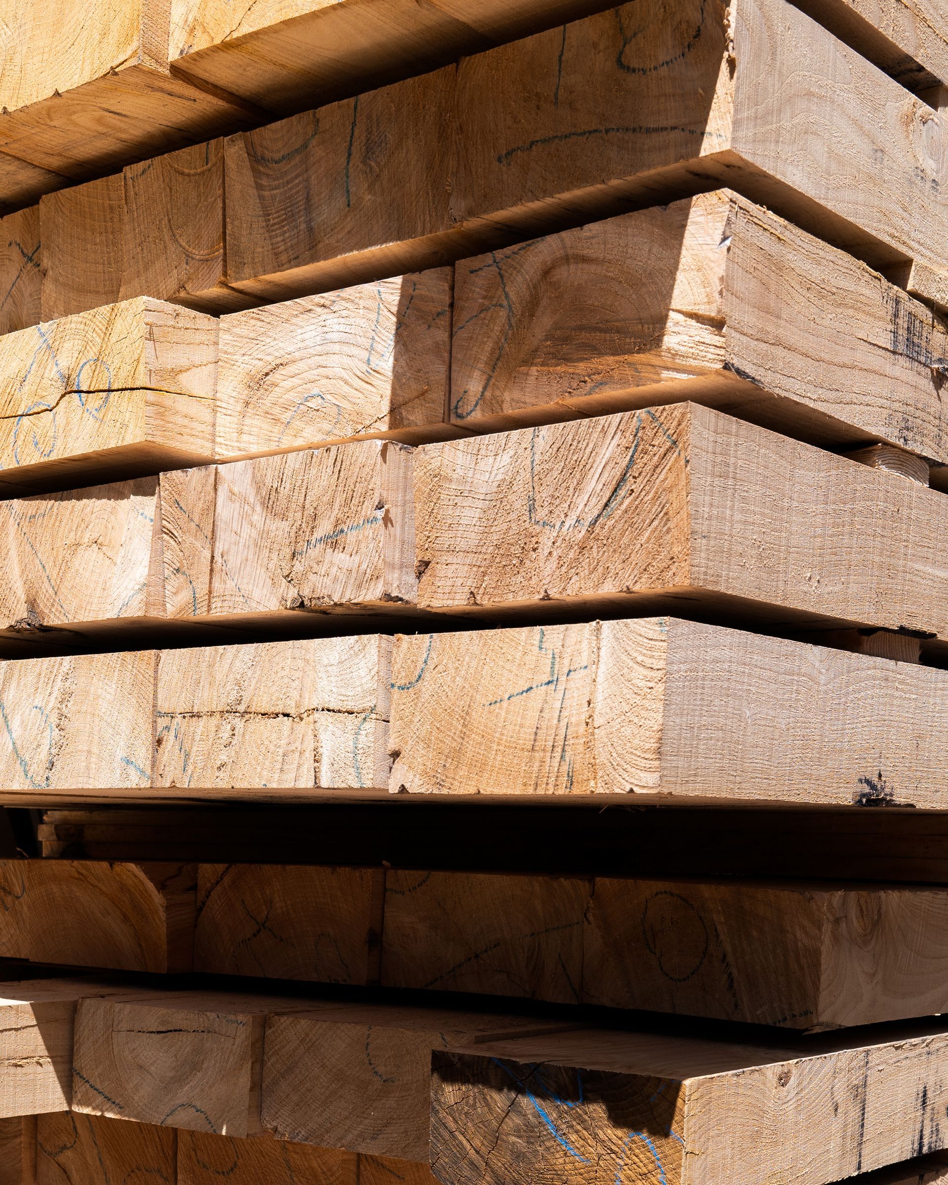Pila di assi di legno rettangolari, color marrone chiaro e marrone, esposte alla luce diretta del sole.