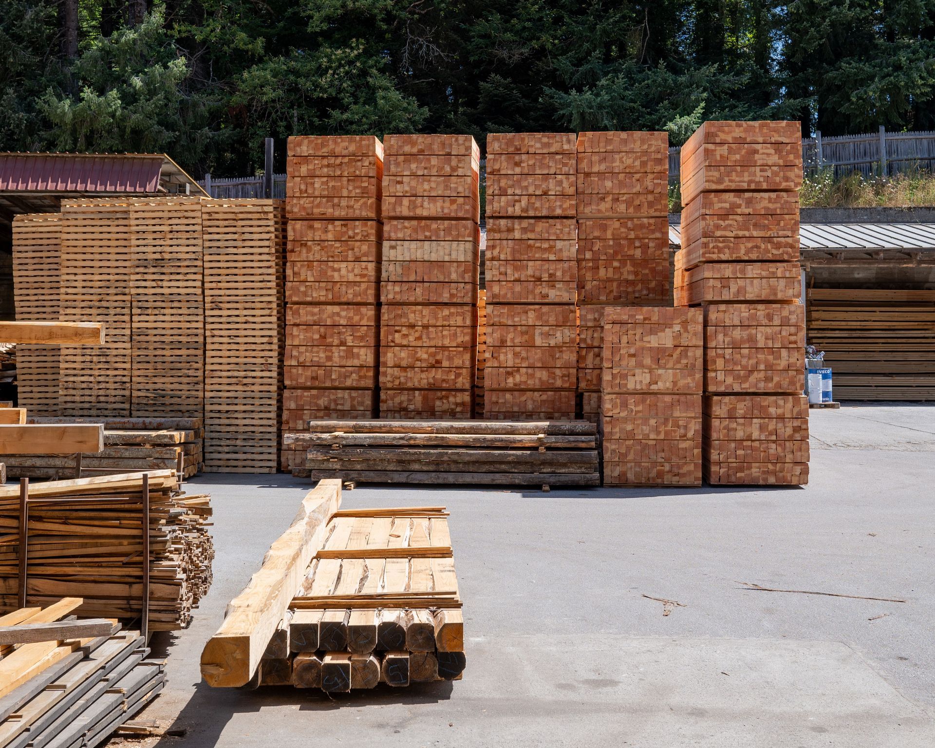 Cataste di legname in un deposito, accatastate in file e pile ordinate, di vari tipi di legno.