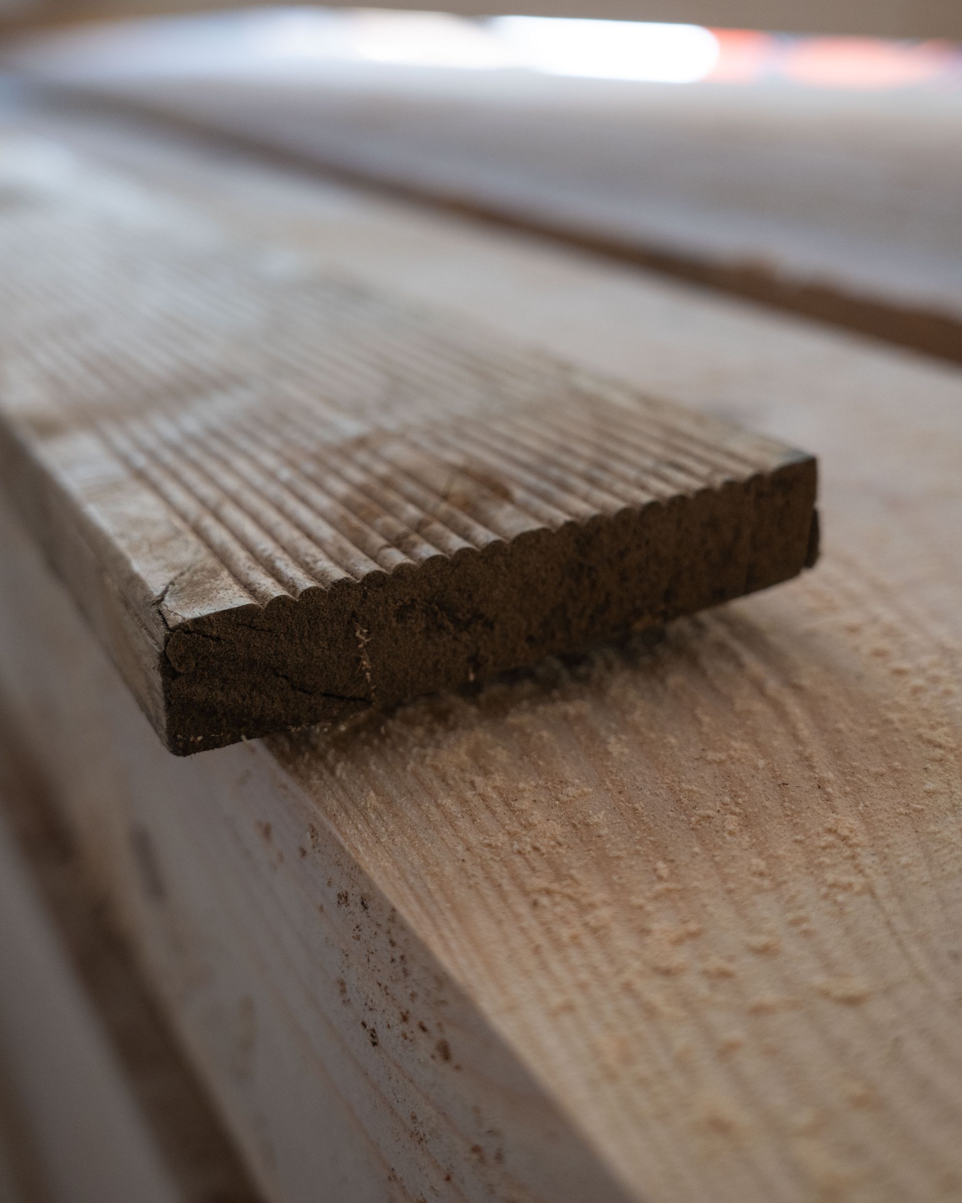 Primo piano di una tavola di legno con venature visibili, appoggiata su una pila di tavole simili.