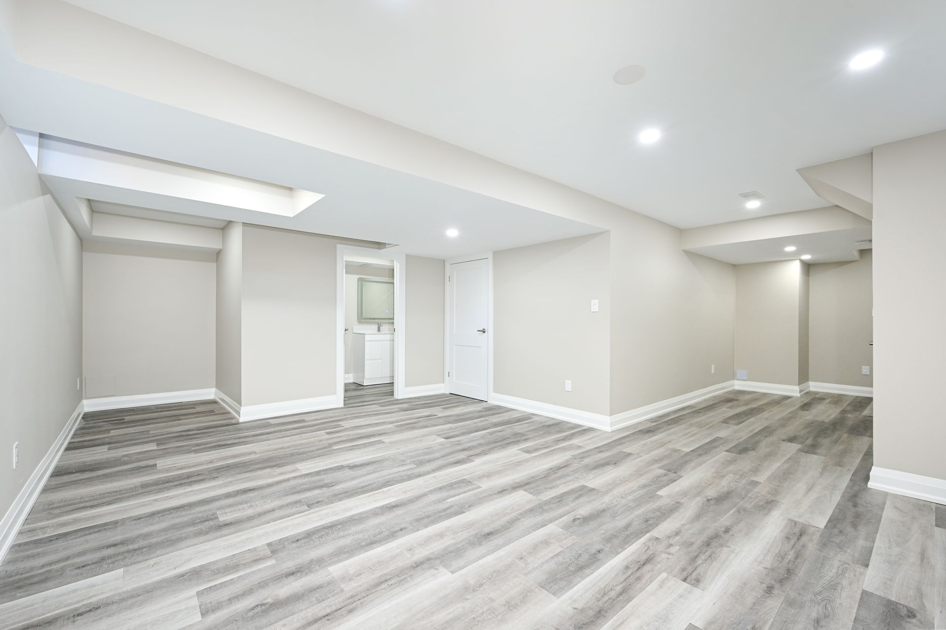 An empty basement with hardwood floors and white walls.