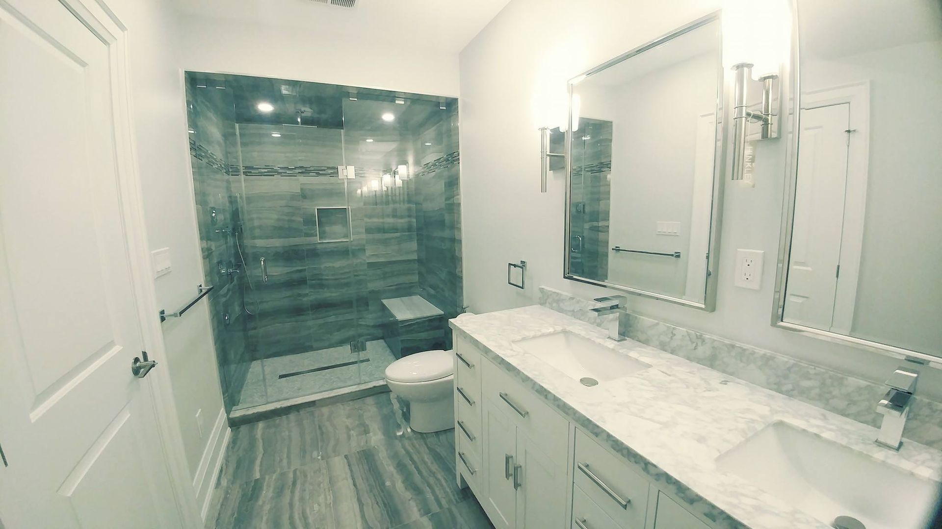 A bathroom with a toilet , sink , mirror and walk in shower.