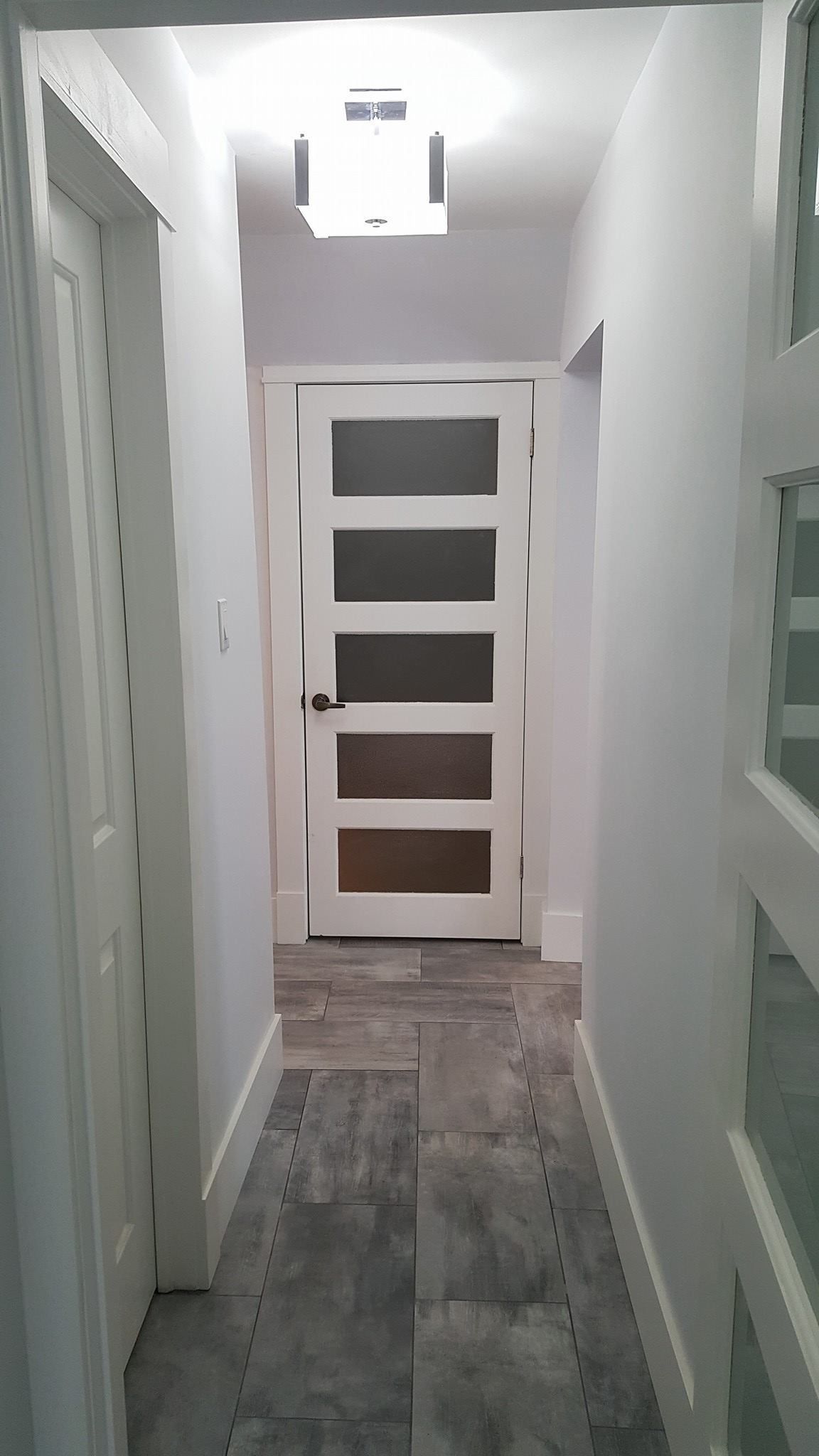 A long hallway with a white door and a light on the ceiling.