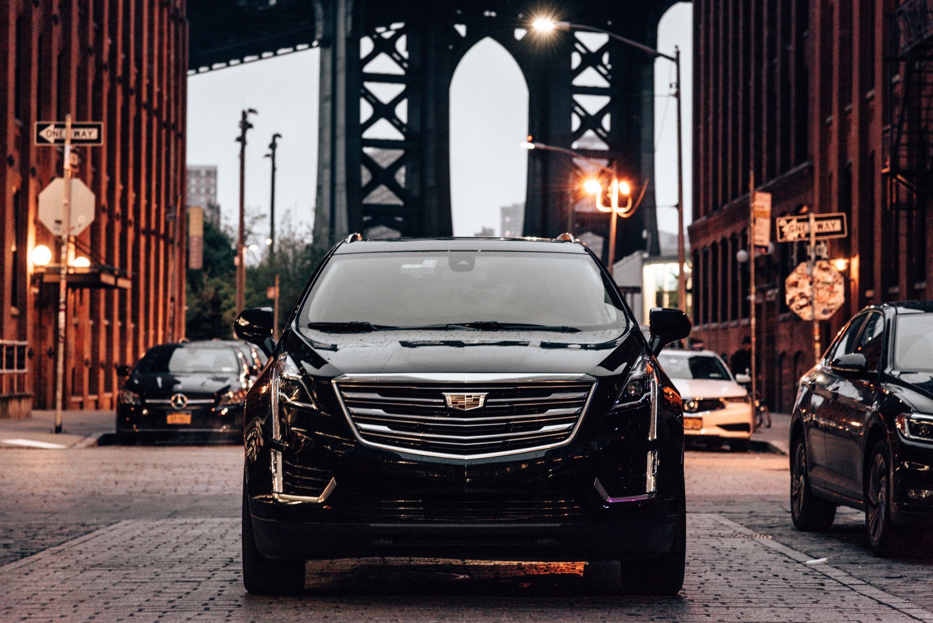 Black Cadillac SUV parked on a cobblestone street, Manhattan Bridge in the background.