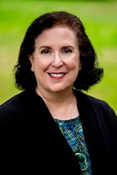 A woman in a black jacket and blue shirt is smiling for the camera,