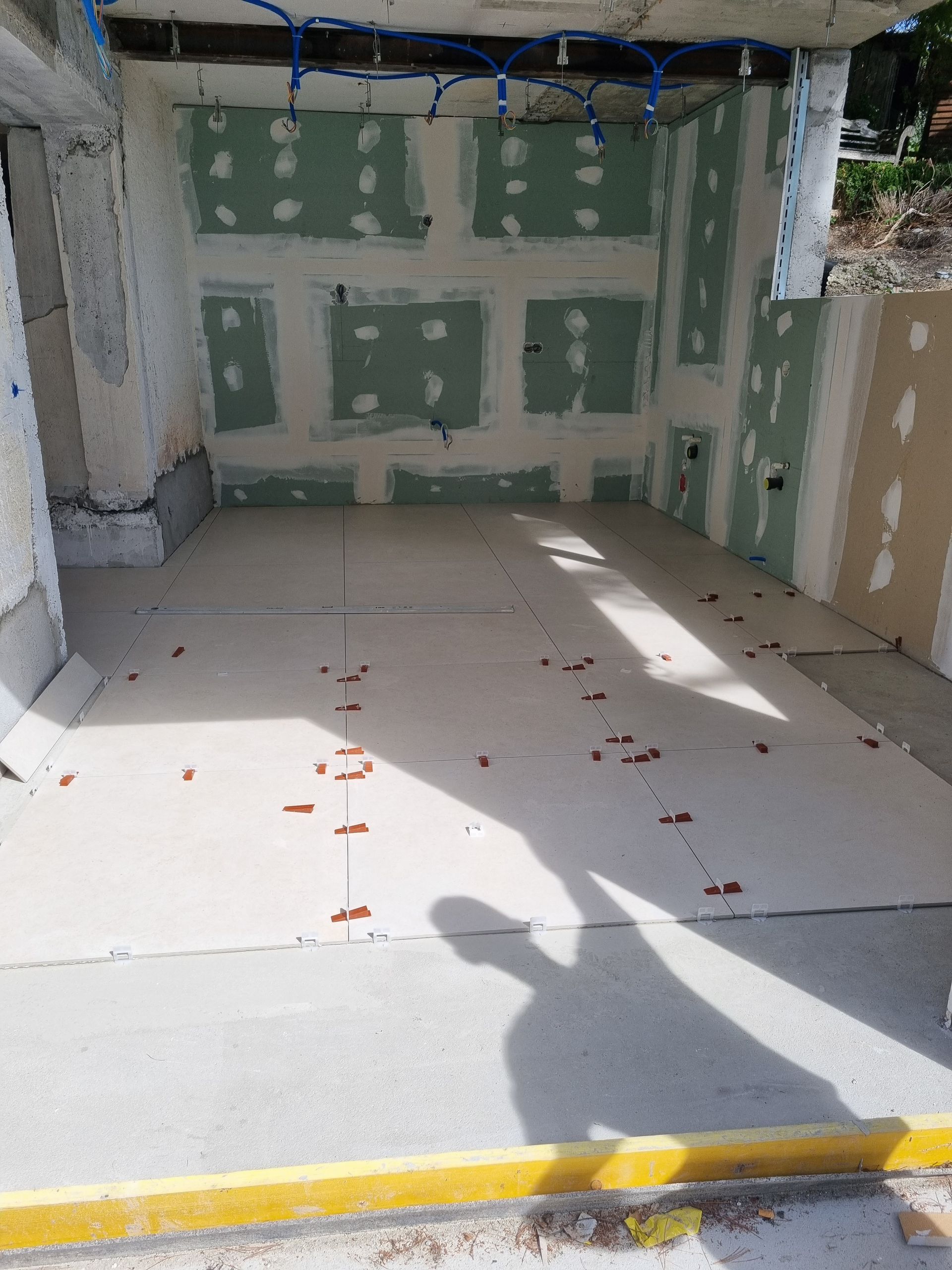 Intérieur d'une pièce inachevée avec des panneaux de plaques de plâtre verts, des panneaux d'isolation au sol et des débris de construction au sol.