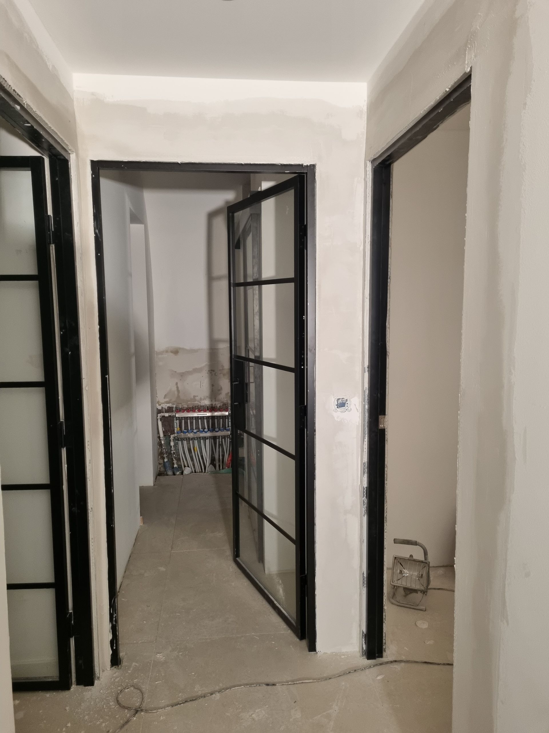 Un couloir en rénovation montrant trois portes vitrées à cadre métallique noir et des cloisons sèches non finies.