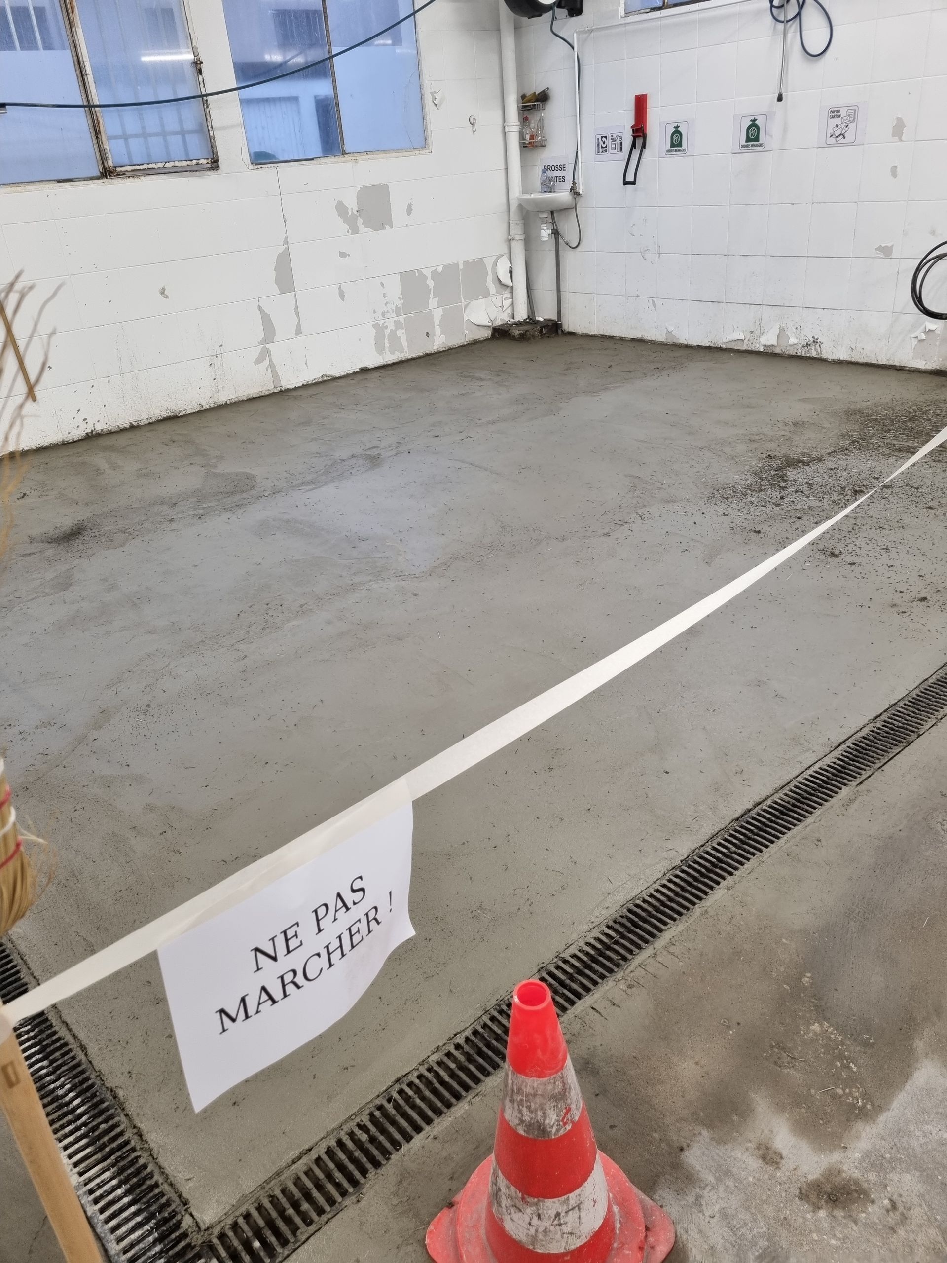 Sol en béton fraîchement coulé, délimité par un panneau indiquant « NE PAS MARCHER » (NE PAS MARCHER) et un cône de sécurité.