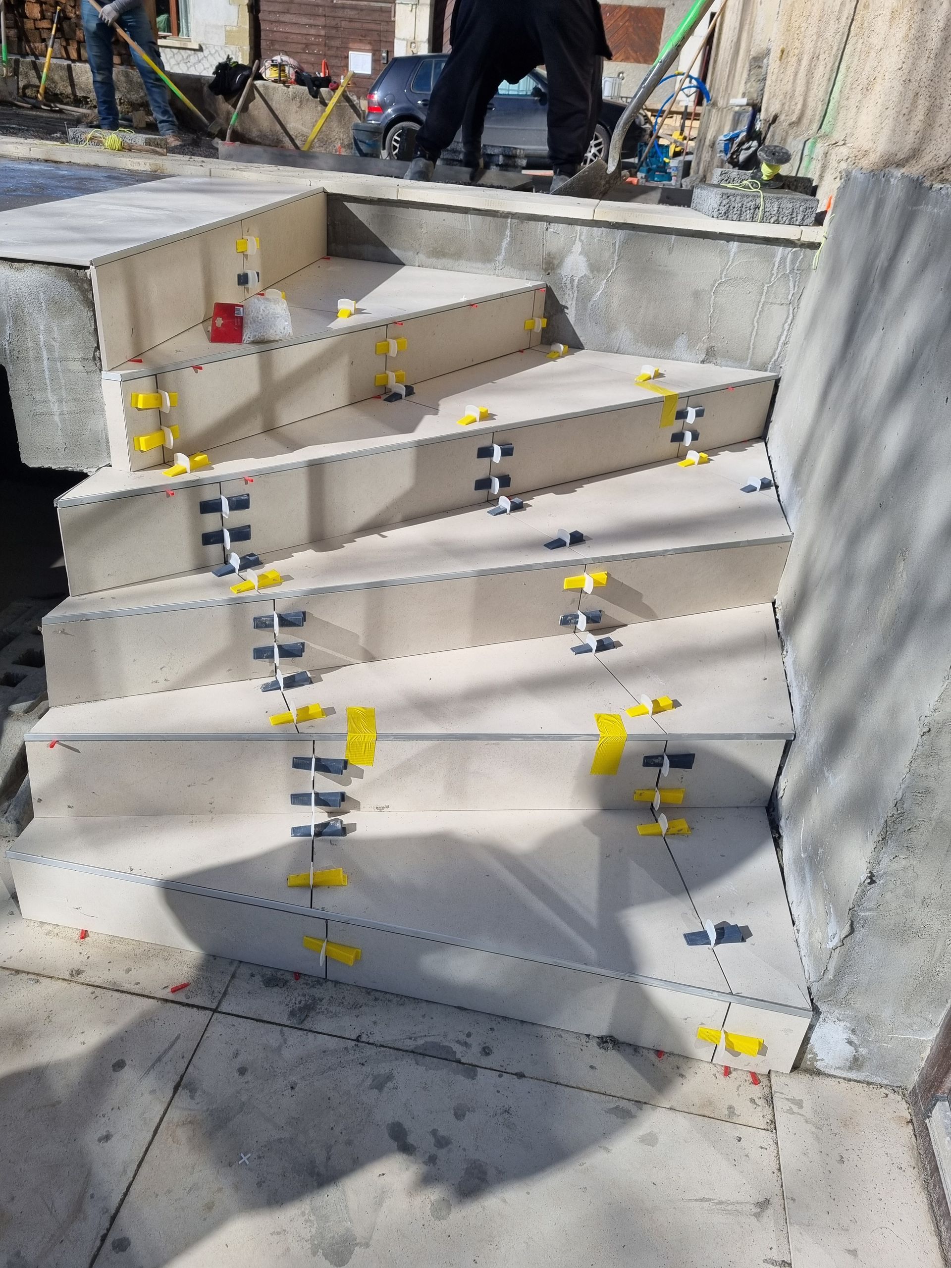 Escalier en pierre claire en construction, avec clips et cales de nivellement pour les carreaux sur les bords.